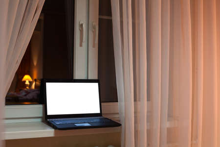 Laptop with cutout screen of monitor laying on windowsill at evening time in a roomの写真素材