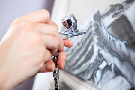 An aerograph unit or paint sprayer in human hand drawing on canvas, close up viewの写真素材