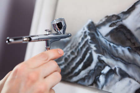 Steel chrome airbrush device in human hand, painting with aerograph, close up viewの写真素材