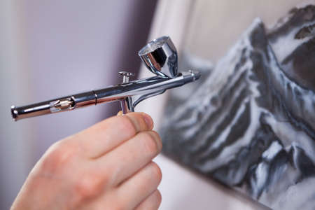 Spraying gun an air brush in female hand, painting mountains with aerograph, close-up viewの写真素材