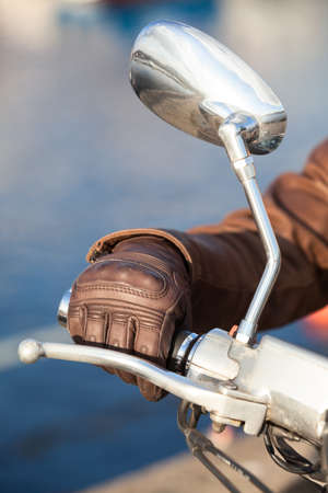 Motorbiker arm in brown leather brown glove holds twist grip throttle, close-up view with mirror