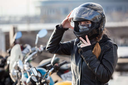 Young European girl biker trying black motorcycle helmet for ride on bikeの写真素材