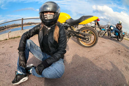 Wide angle of girl motorcycle rider sitting on earth next to her bike and female biker with chopper...
