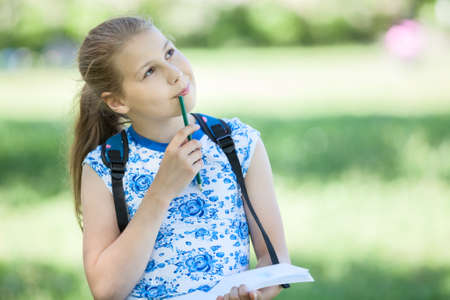 Small thoughtful girl standing in park with sketchbook and pencil in hands, copyspaceの写真素材