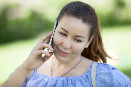 Head and face portrait of beautiful European young woman talking by cellphone on nature