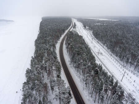 Aerial view at parallel highway and railroad range winter sea coast. Snowy blizzard weather. View from flying droneの写真素材