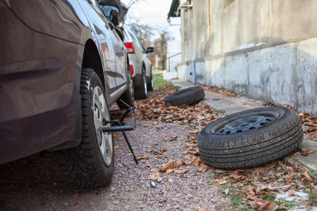 Summer tire wheels changing to snow studded tyres at autumn season. Backyard of house