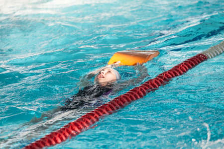 Young Caucasian girl sportsman swiming backstroke with kickboard in poolの写真素材