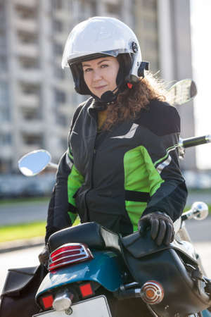 Portrait of motorbiker Caucasian woman in white open face crash helmet and touring jacket sitting on...
