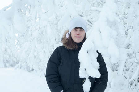 Young European woman portrait standing on snowy road with snow-capped tree branches