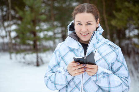 Portrait of Caucasian young woman holding smartphone in hands. Winter forestの写真素材