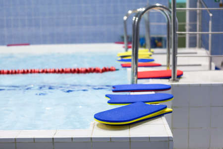 Bright color swimming boards laying at edge of small indoor poolの写真素材