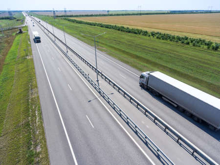 Long vehicle semi-trailer truck driving on straight four lanes highway passing in meadowsの写真素材