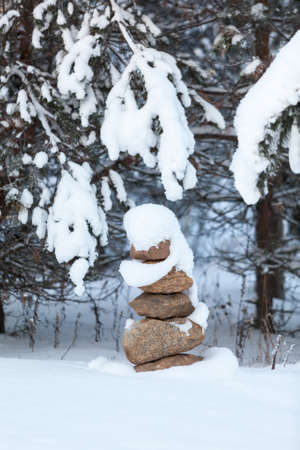 Pyramid from pebbles as tower in wintry forest under branches covered with lot of snowの写真素材