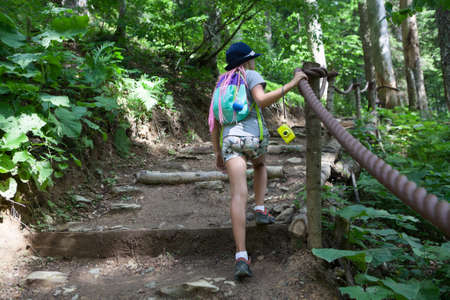 European girl climbs up natural stairs in summer forest, hiking route, rear view, copyspaceの写真素材