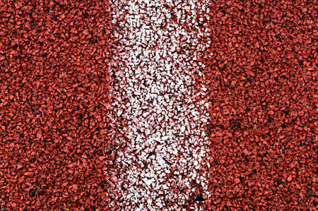 Close-up view at red rubber running line with vertical white stripe in the middle, background