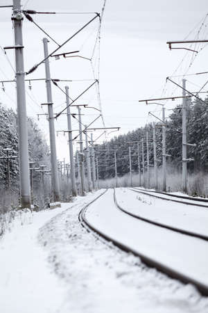 Electrified railway line with poles for wires at winter season, empty roadの写真素材