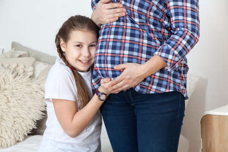Happy and smiling teen age daughter listen belly of pregnant mother, touching with handsの写真素材