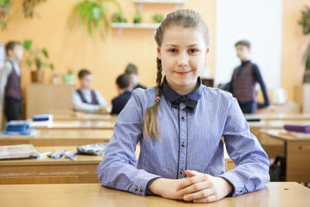 Primary school student sitting at table in classroom at recess time, portrait of preteen Caucasian girlの写真素材