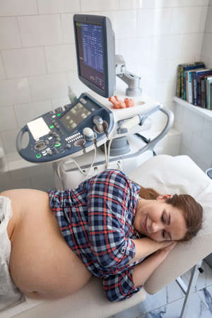 Happy pregnant European woman before getting ultrasound scan from obstetrician in clinic, lying lateral positionの写真素材