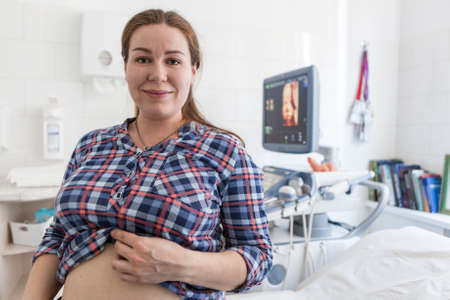 Pregnant woman happy with the result of ultrasonography, standing in hospital room with 3d model of...