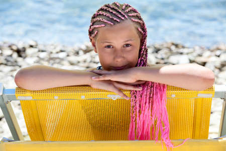 Facial portrait of pre-teen Caucasian girl with pink dreadlocks hairstyle looking out from yellow...