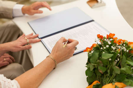 Close-up view of female hands signing wedding certificate at marriage, mature people armsの写真素材