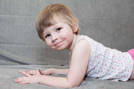 Four years old Caucasian girl dressed shirt lying on sofa, looking at camera