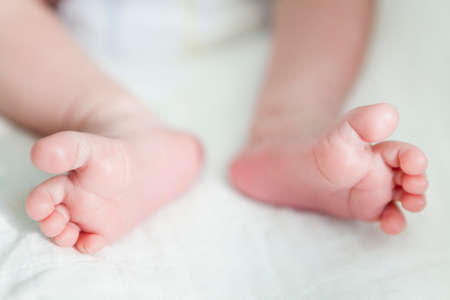 Small legs of baby, lying on white linen in bed, close up view