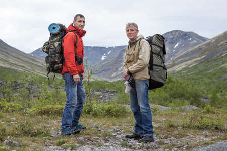 Two backpackers hiking in mountains. Senior and young adult men looking at camera togetherの写真素材