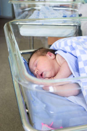 Cute Caucasian little newborn baby sleeping in hospital bed, folded hands with open mouth, lying under blanketの写真素材