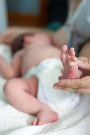 Newborn infant barefoot leg in women hand, mother breastfeeding baby lying in bed, close-up viewの写真素材