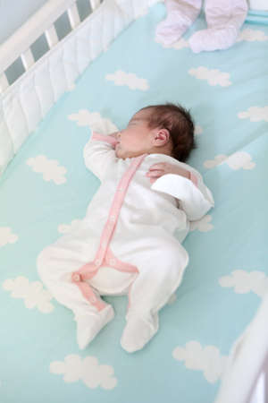 Baby girl with white and pink clothes asleep in a wooden bed