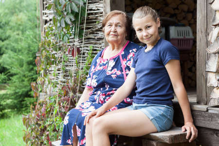 Preteen girl a granddaughter sitting on stairs with her grandma, timber house in forest, copyspaceの写真素材