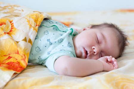 Infant sleep covered with a blanket, large bed, closed eyes and hand upの写真素材