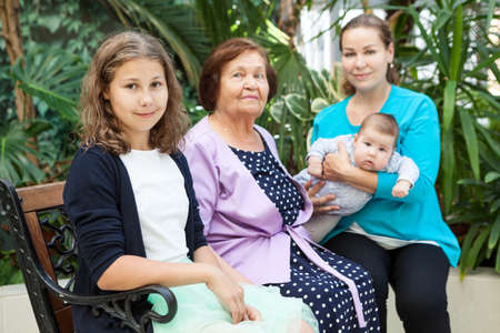 Young woman holds a baby in her arms, sitting next to her preteen daughter and grandmotherの写真素材