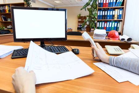 Engineer work place with blueprint, telephone and blank white display of pc monitor, first person...