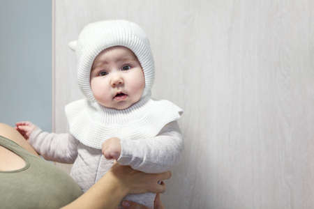 Mother holding her daughter on arms with dressed warm children bonnet, copy space
