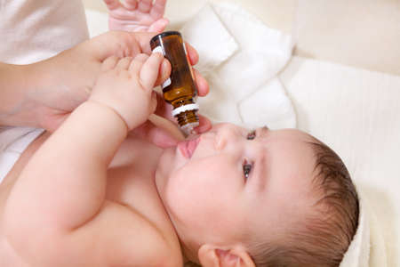 Mother hands giving glass bottle with vitamin D or B6. Baby getting drops oralの写真素材