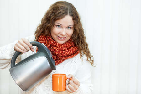 Curly hair smiling woman pouring hot water from kettle into orange bowl.の写真素材
