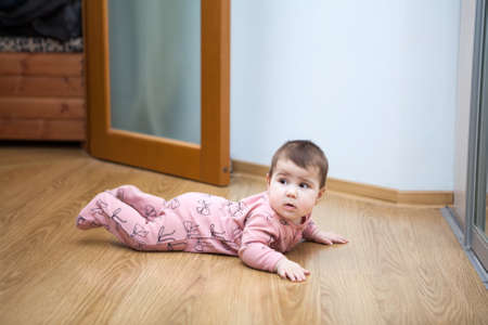Six month baby trying to creep on laminate floor in domestic room, side view