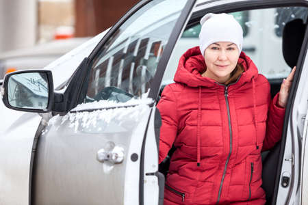 Attractive woman dressed red jacket and white hat sitting at driver seat in her car with opened...