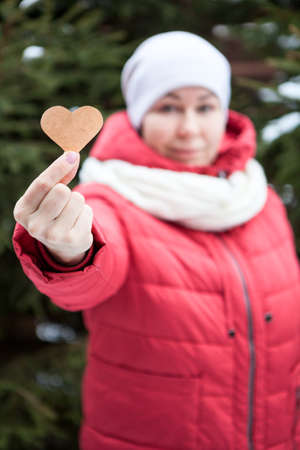 Adult woman showing heart shape in stretched hand, red jacket, white scarf and hat, blurred headの写真素材