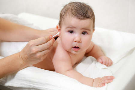 Female hands cleaning baby ears with cotton swab, infant hygiene after showerの写真素材