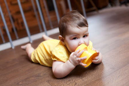 Baby child nibbling plastic block of pyramid, teething problems. Domestic room with hardwood floor