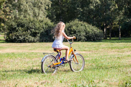 Young girl in white dress riding her bicycle in summer park on meadow with green grassの写真素材
