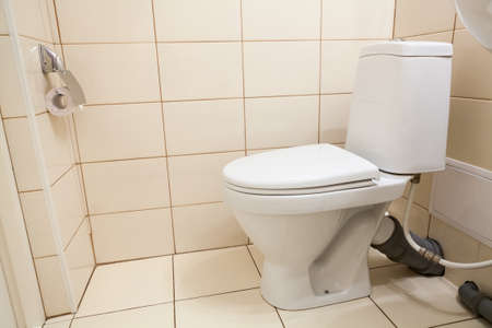 Clean white bathroom toilet with the lid closed and hanging paper roll holder, side view