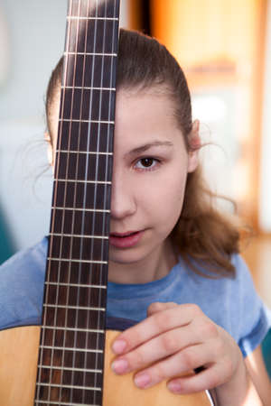 Portrait of teenage girl guitarist with fretboard of guitar, looking at cameraの写真素材