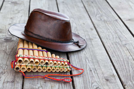 Multiple pipes pan flute and leather cowboy brown hat lying on square-edged flooring, copy space