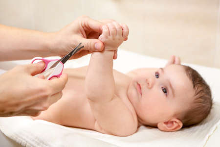 Baby getting fingernails cut by his mother with scissors while lying on his back. Nursing a childの写真素材
